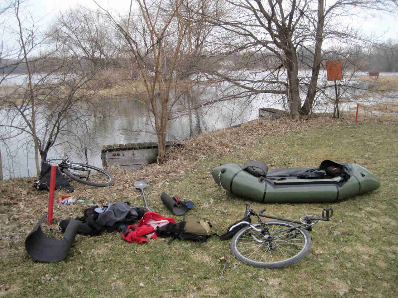 Surly Travelers Check bike parts, an inflatable raft, and gear, on a flat grassy area, with a lake in the background